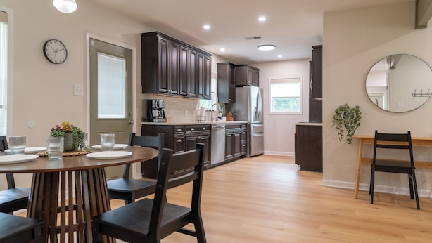A modern kitchen with dark cabinets, a refrigerator, a coffee maker, and a dining area with a round table and chairs. - Charming 2-bedroom 2-bath house close to Texas State University and the River (San Marcos)