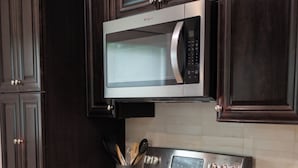 A kitchen with dark wood cabinets, a stainless steel microwave, and an oven. - Charming 2-bedroom 2-bath house close to Texas State University and the River (San Marcos)