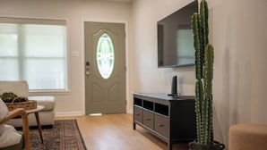 A living room with a wooden floor, a sofa, a coffee table, a television on a stand, and a cactus plant. - Charming 2-bedroom 2-bath house close to Texas State University and the River (San Marcos)