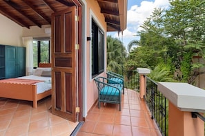 Ein Balkon mit einem Bett, einem Stuhl und Blick auf Grünflächen.