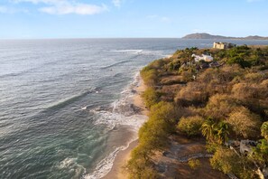 Blick auf die Küste mit Strand, Vegetation und einem Gebäude in der Ferne.