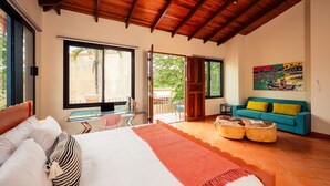 Ein Schlafzimmer mit einem Bett, einem Schreibtisch, einem Laptop, einem Sofa und einem Gemälde.
