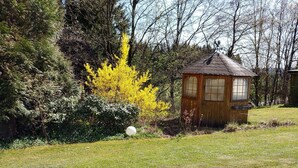 Eine kleine Holzhütte mit geneigtem Dach, umgeben von dichtem Grün und Bäumen.