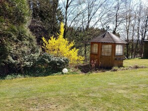 Eine kleine Holzhütte mit geneigtem Dach, umgeben von dichtem Grün und Bäumen.