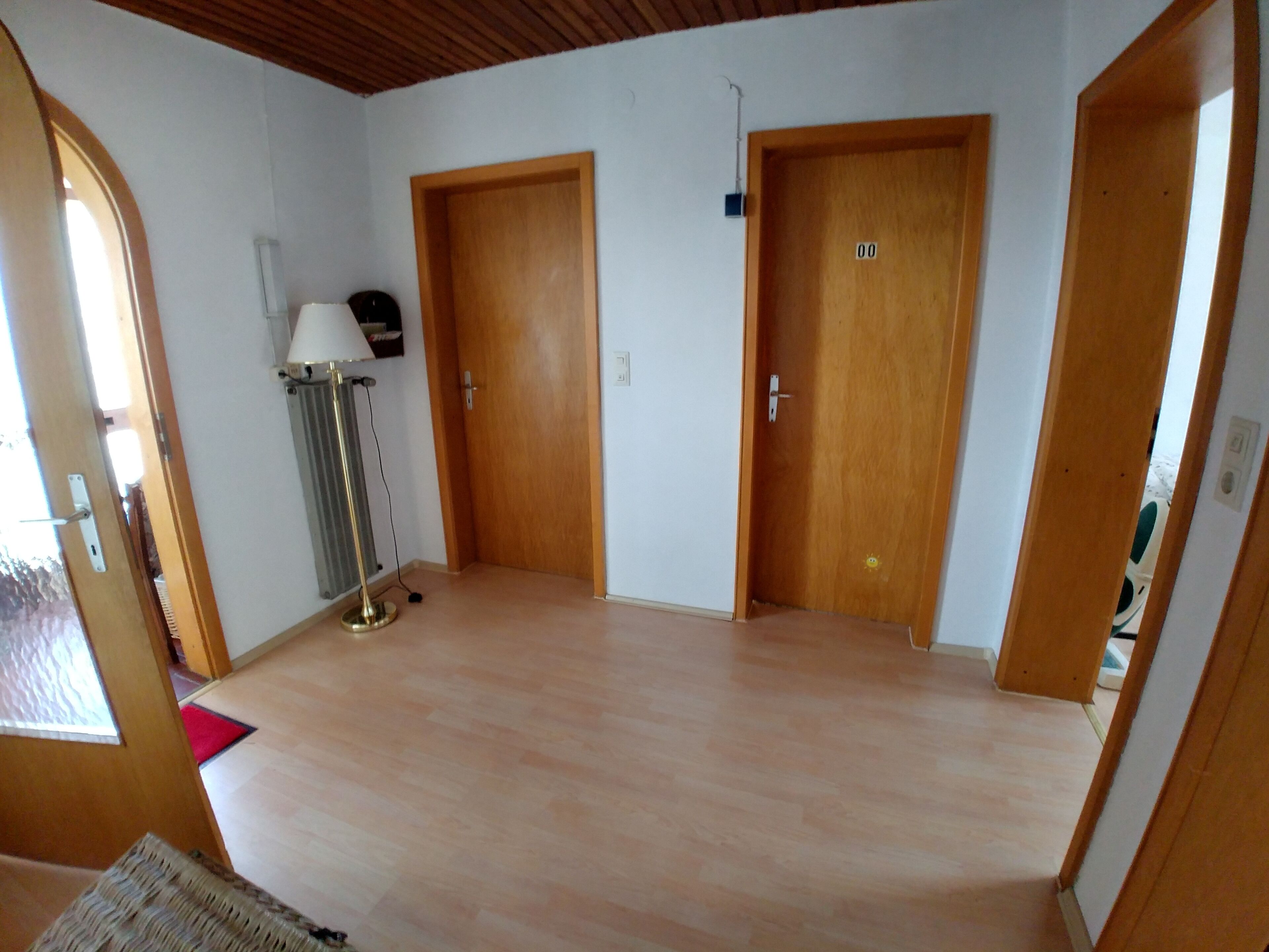 A room with wooden flooring, two wooden doors, a standing lamp, and a radiator.
