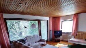 Ein Wohnzimmer mit einer Couch, einem Fernseher und einem Fenster mit Vorhängen.