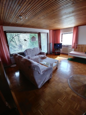 Ein Wohnzimmer mit einer Couch, einem Fernseher und einem Fenster mit Vorhängen.
