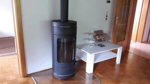 Ein Zimmer mit Kaminofen, einem weißen Tisch mit Glas und einer kleinen Ablage mit Gegenständen.