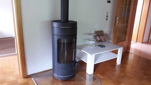 Ein Zimmer mit Kaminofen, einem weißen Tisch mit Glas und einer kleinen Ablage mit Gegenständen.