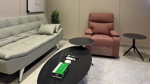 Een moderne woonkamer met een grijze bank, een roze fauteuil, een zwarte salontafel en een kleine ronde tafel.