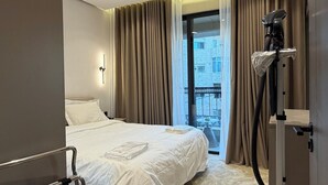Hotelkamer met een bed, een stofzuiger, een raam met gordijnen en uitzicht op gebouwen.