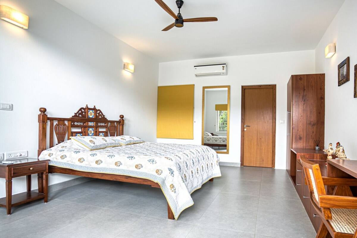 A bedroom with a wooden bed, bedside tables, a ceiling fan, an air conditioning unit, and a wooden wardrobe.