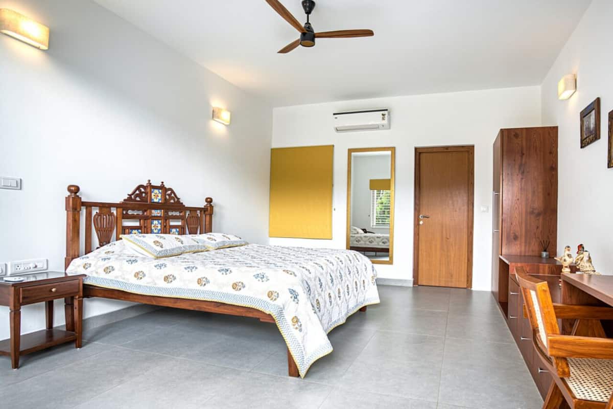 A bedroom with a wooden bed, bedside tables, a ceiling fan, an air conditioning unit, and a wooden wardrobe.