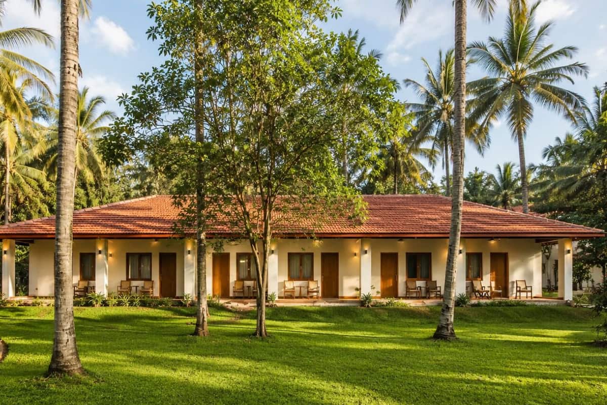 A two-story building with a red-tiled roof, multiple rooms with doors, and a well-maintained lawn with palm trees.
