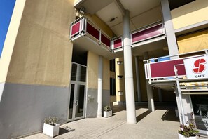 Un bâtiment avec une enseigne indiquant la présence d’un café, une entrée avec une porte vitrée et un balcon agrémenté de coussins rouges.