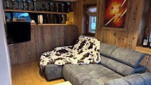 Uma sala de estar aconchegante com um sofá cinzento, um banquinho branco e uma parede de madeira com troféus.