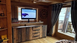 Interior em madeira com televisão, armário de madeira e janela com cortinas.