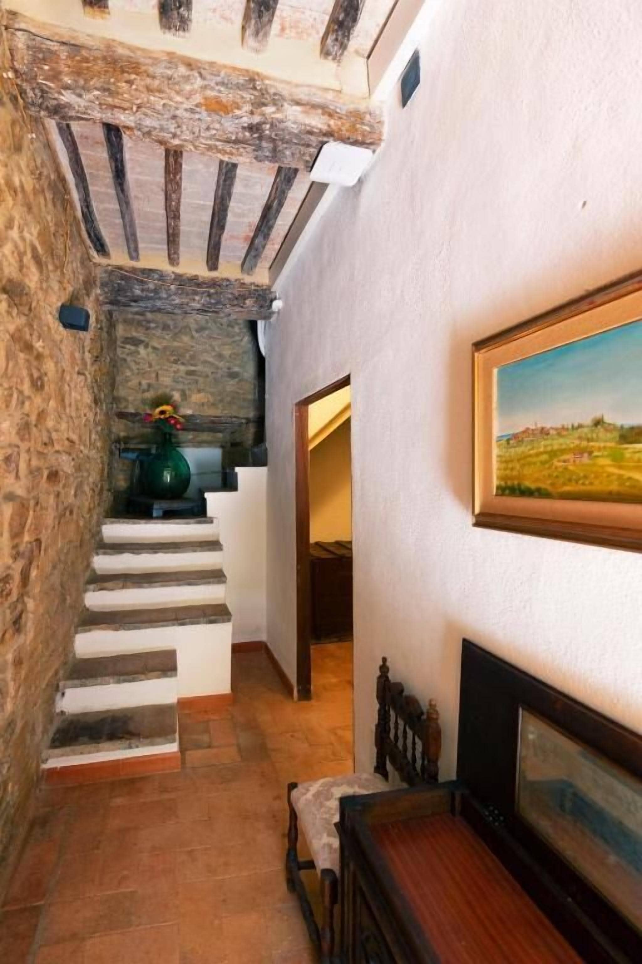 A narrow hallway with stone walls, a wooden staircase, a framed painting, and a radiator.