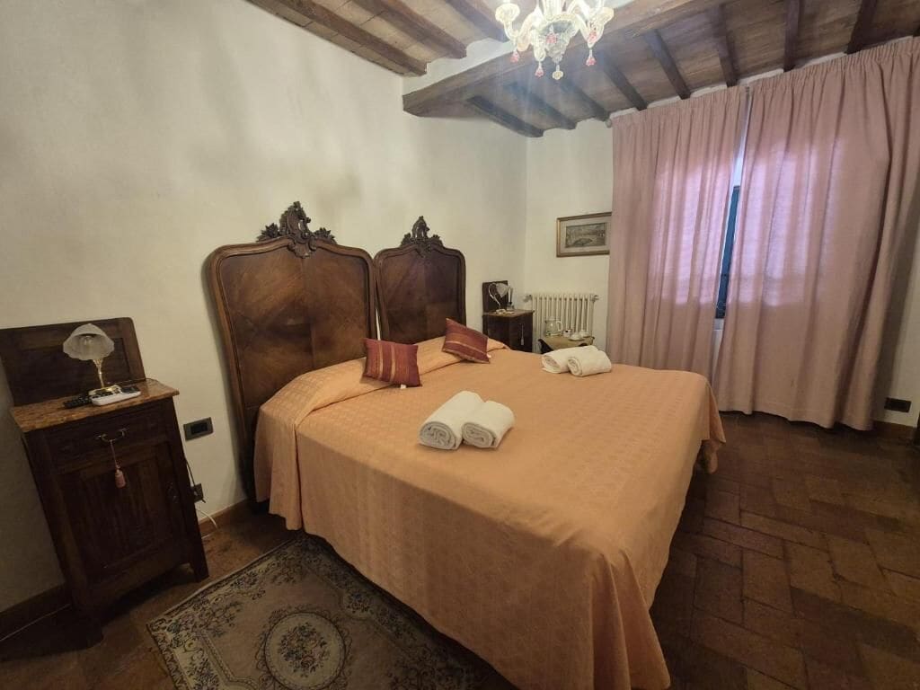 Une chambre à coucher avec un lit en bois, une table de chevet, une lampe, un radiateur et une fenêtre avec des rideaux.