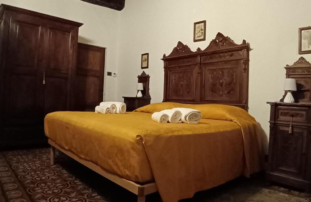 A room with a bed, wooden wardrobe, and a nightstand with a lamp.