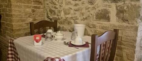 A stone-walled room with a table set for dining, featuring a checkered tablecloth and wooden chairs.