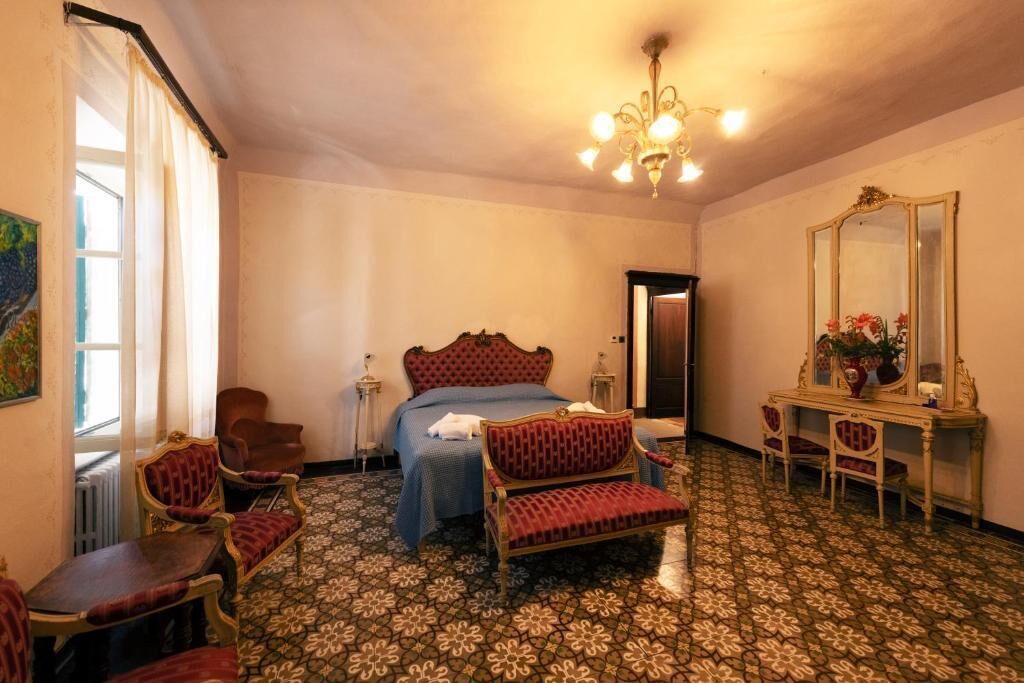 A hotel room with a bed, two chairs, a table, a mirror, and a chandelier.