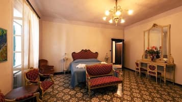 A hotel room with a bed, two chairs, a table, a mirror, and a chandelier.