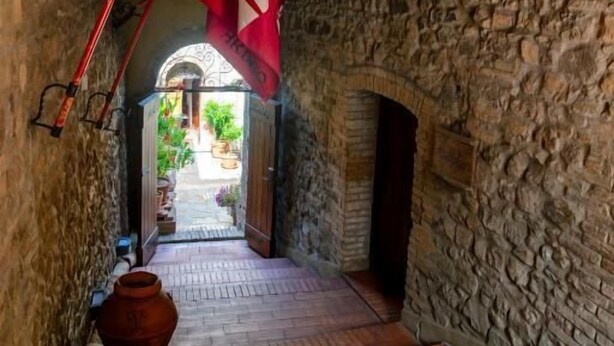 Un pasillo de paredes de piedra con suelo de madera, una bandera roja y vistas a un patio.