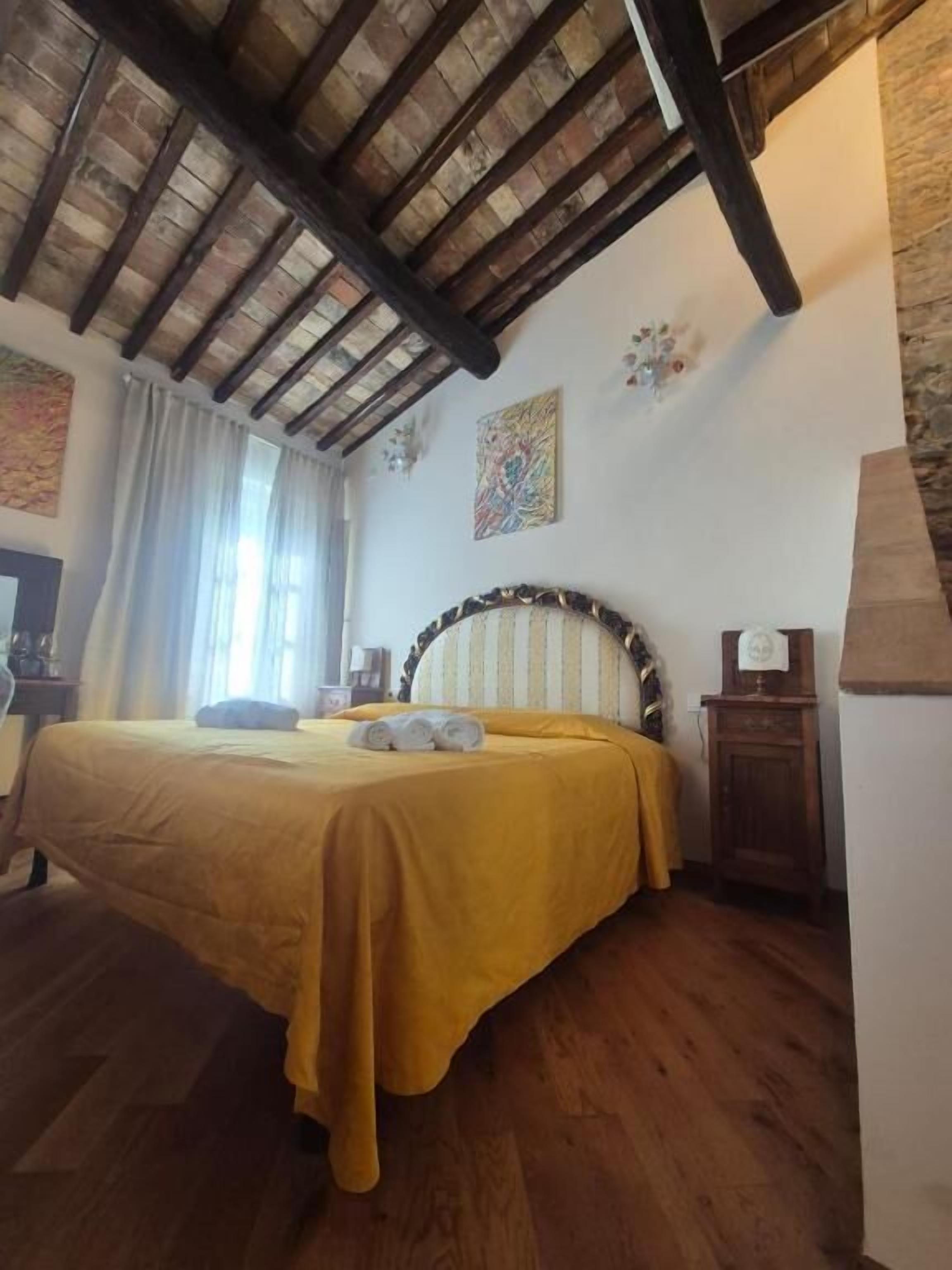 Une chambre à coucher avec un plafond en bois, un lit recouvert d’une couvre-lit jaune, une table de chevet et une lampe fixée au mur.