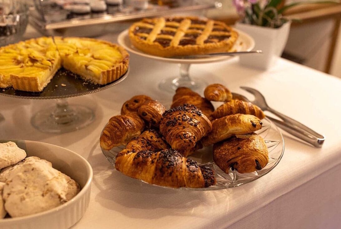 A buffet table with a variety of baked goods including pies, croissants, and ice cream.