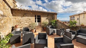 Un edificio de piedra con un patio empedrado, muebles de mimbre y plantas en macetas.