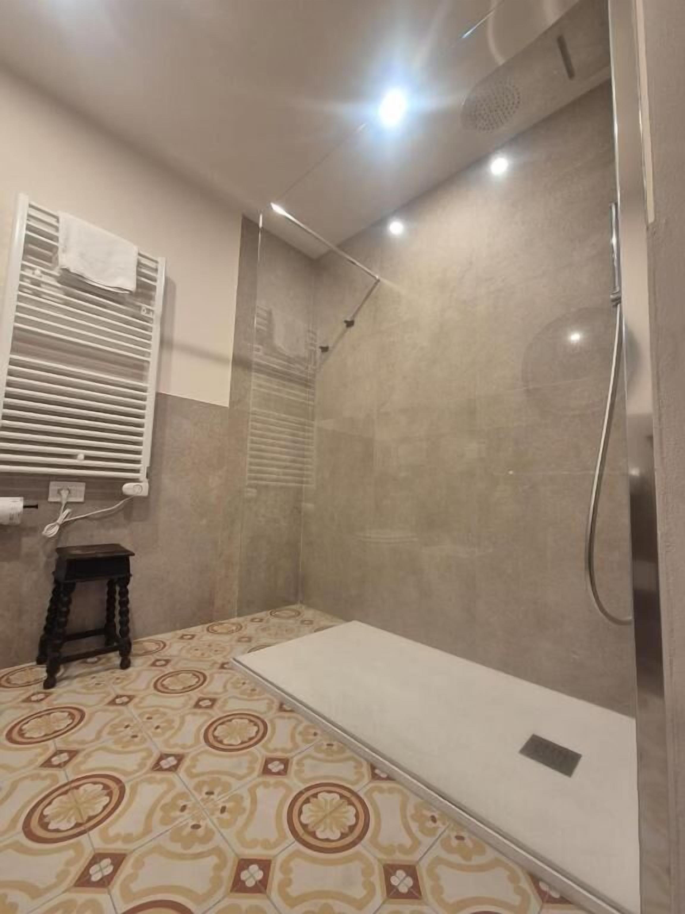 A shower area with a glass door, a small stool, and a patterned floor.