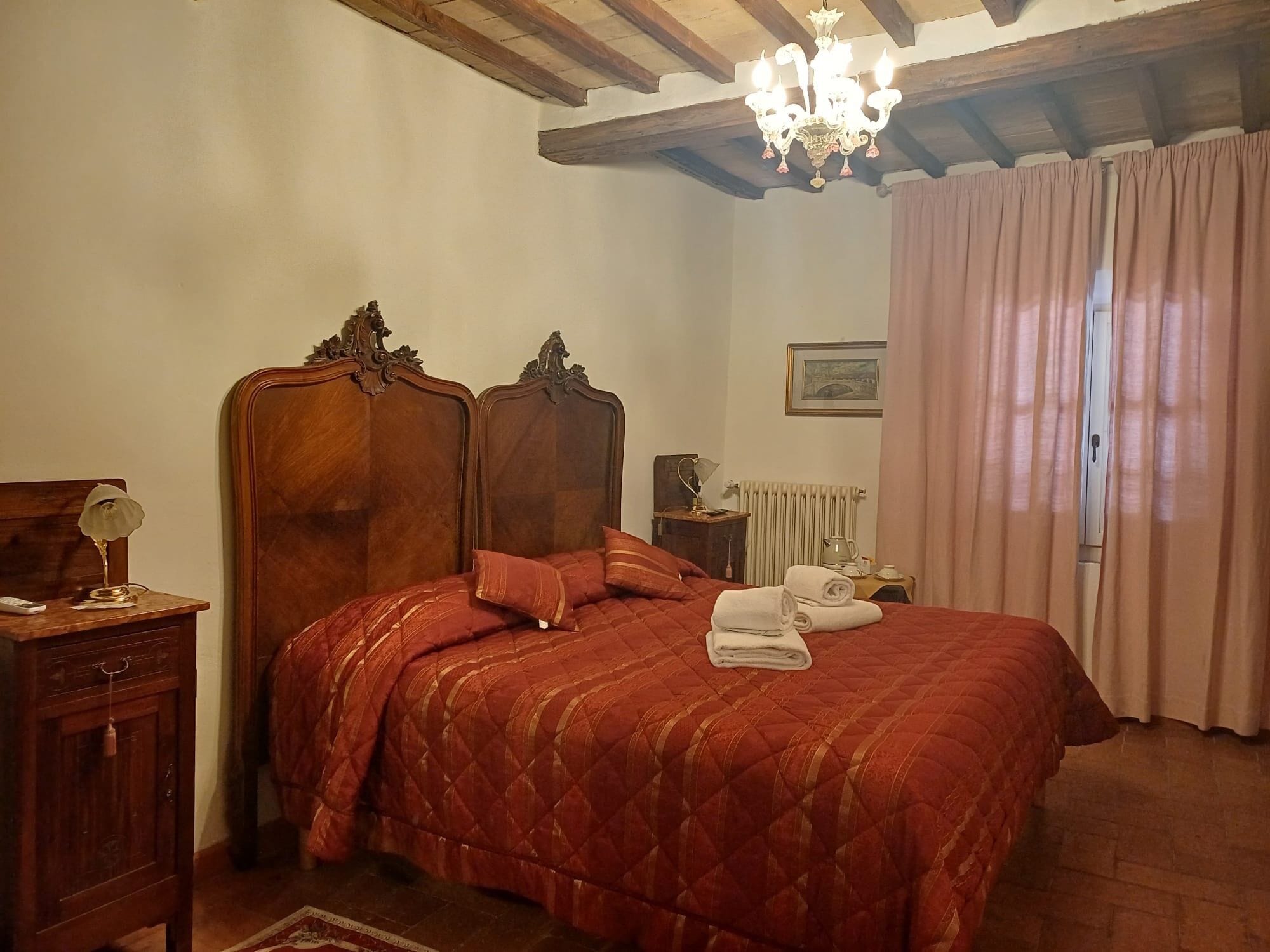 A bedroom with a wooden bed, a chandelier, a radiator, and a window with curtains.