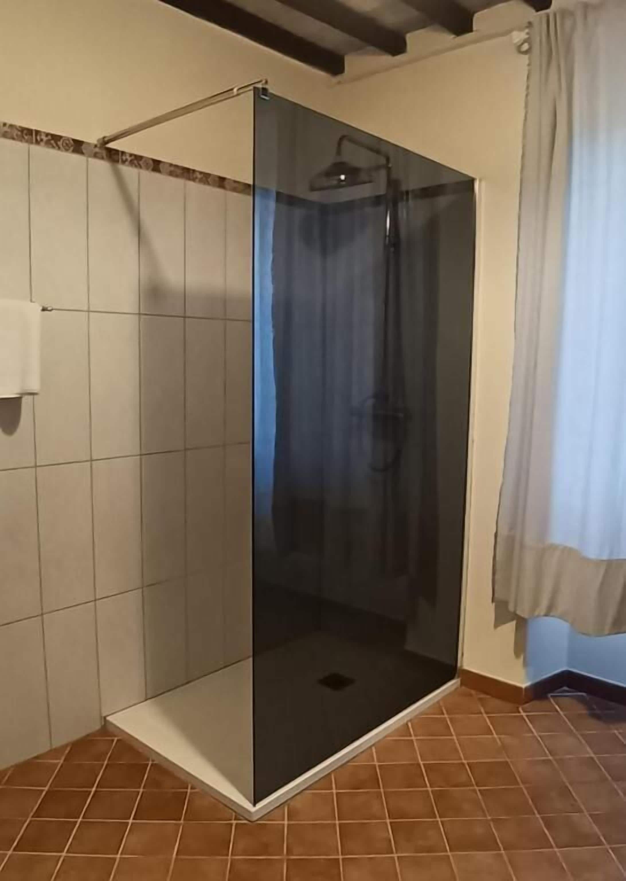 Um chuveiro com paredes de vidro, chão ladrilhado e porta-toalhas.