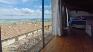 Una habitación con un ventanal grande, suelo de madera y una cama con una colcha azul.