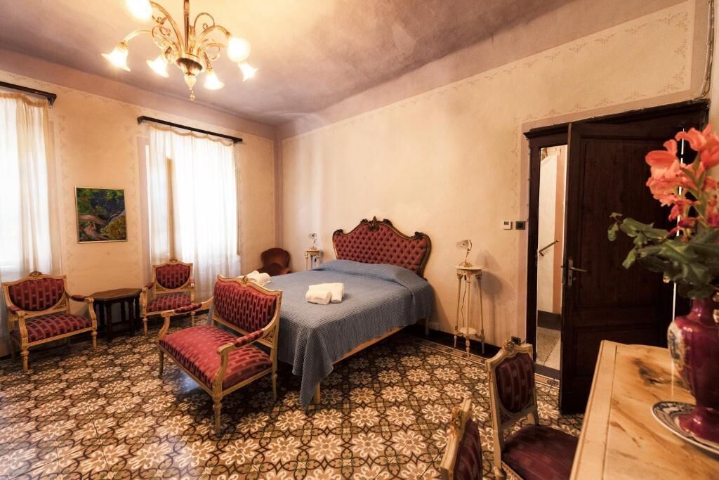 Una habitación con cama, dos sillas, una mesa, una araña y una puerta.