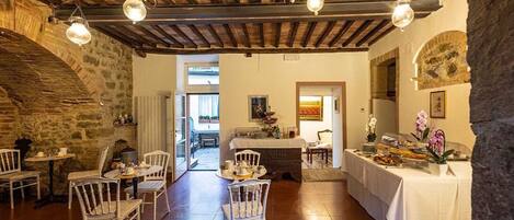Un comedor rústico con vigas de madera, paredes de piedra y sillas blancas.