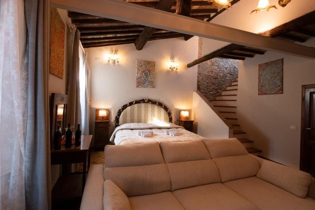 A bedroom with a bed, a sofa, a staircase, and wall-mounted lights.