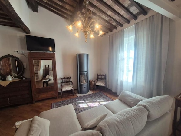 A living room with a sofa, a television, a fireplace, and a chandelier. - PALAZZO DEL CARDINALE (Montalcino)