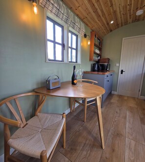 A dining area with a wooden table and chairs, a radio, a bottle, and a glass set.