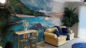 Ein Wohnzimmer mit Wandgemälde von einem Strand, einer Couch, einem Couchtisch und einem Essbereich.