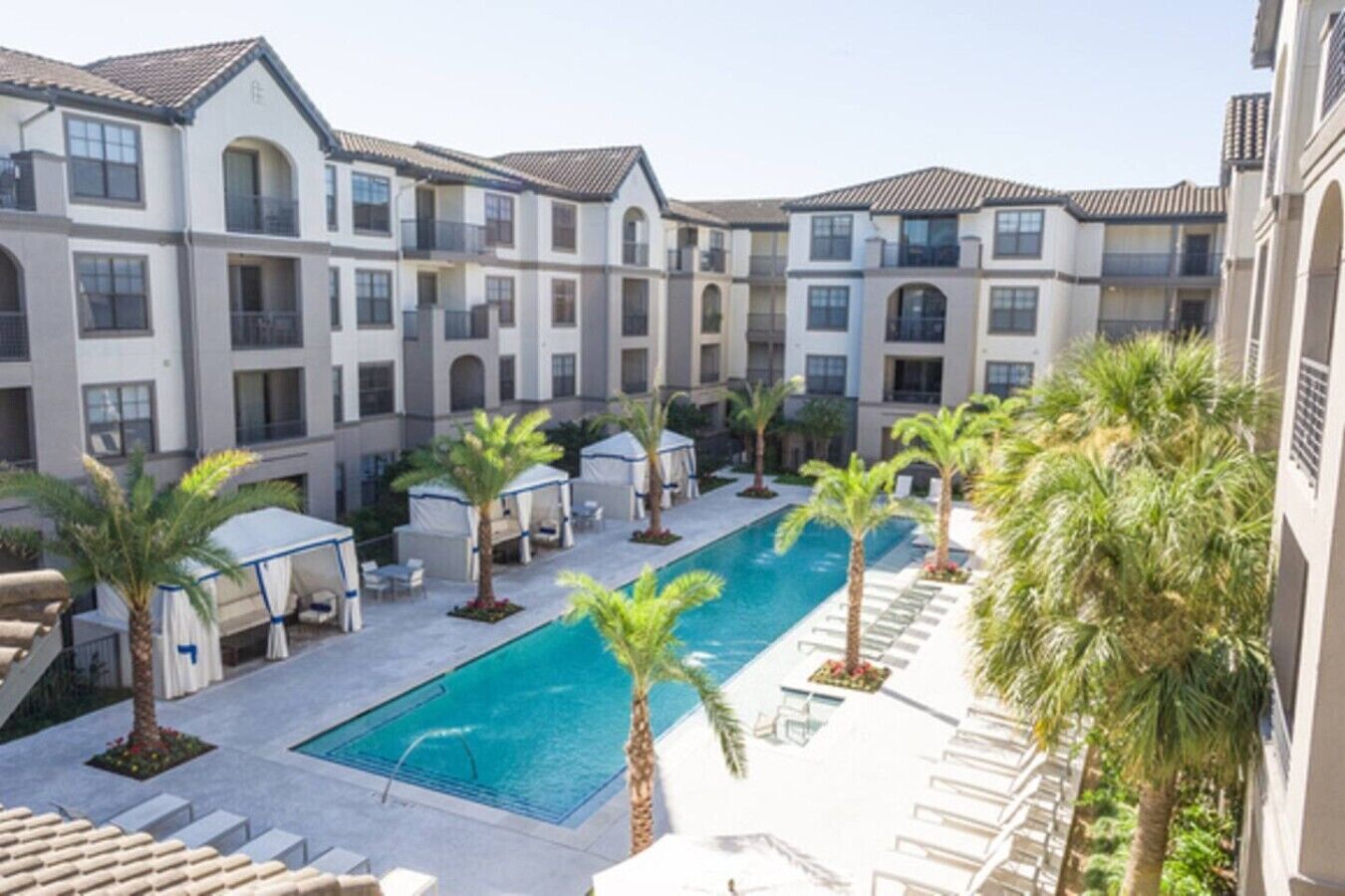 Un patio de hotel con piscina, palmeras y zonas de estar al aire libre.