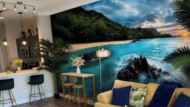 Ein Wohnzimmer mit einer Couch, einem Couchtisch, einem Bild von einer Strandansicht und einer Bar mit Hockern.