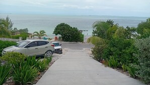 Un camino pavimentado que lleva a una playa, con coches aparcados y abundante vegetación.