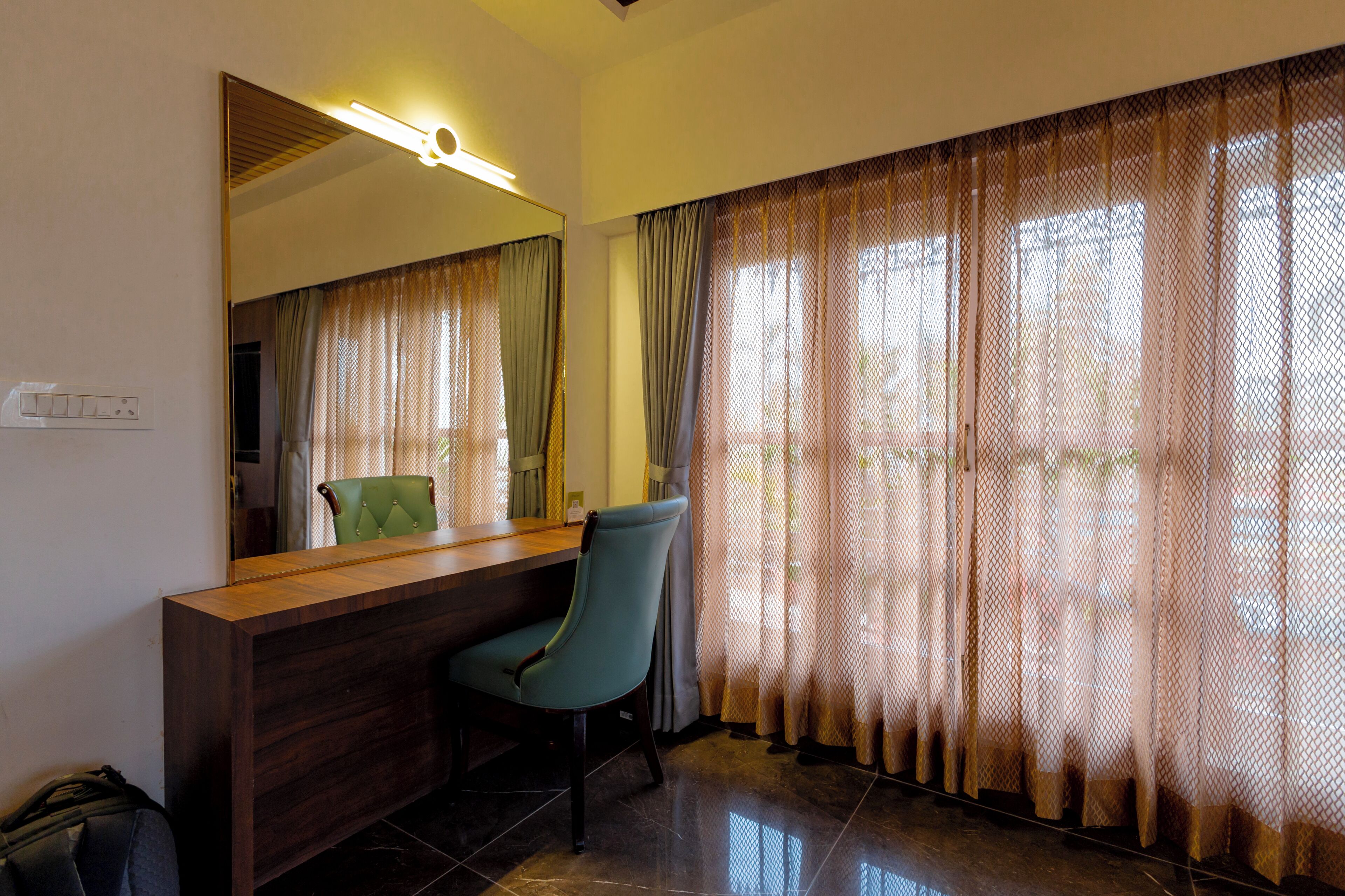 Una habitación con mostrador de recepción de madera, una silla verde, un espejo grande y una ventana con cortinas estampadas.