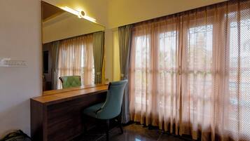 A room with a wooden reception desk, a green chair, a large mirror, and a window with patterned curtains.