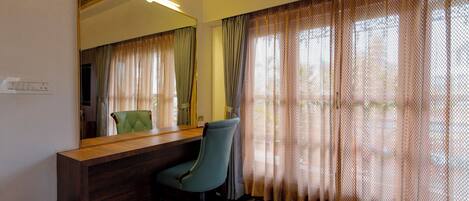 Una habitación con mostrador de recepción de madera, una silla verde, un espejo grande y una ventana con cortinas estampadas.