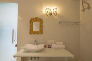 Un baño con un lavamanos blanco, un espejo con marco dorado e iluminación en la pared.