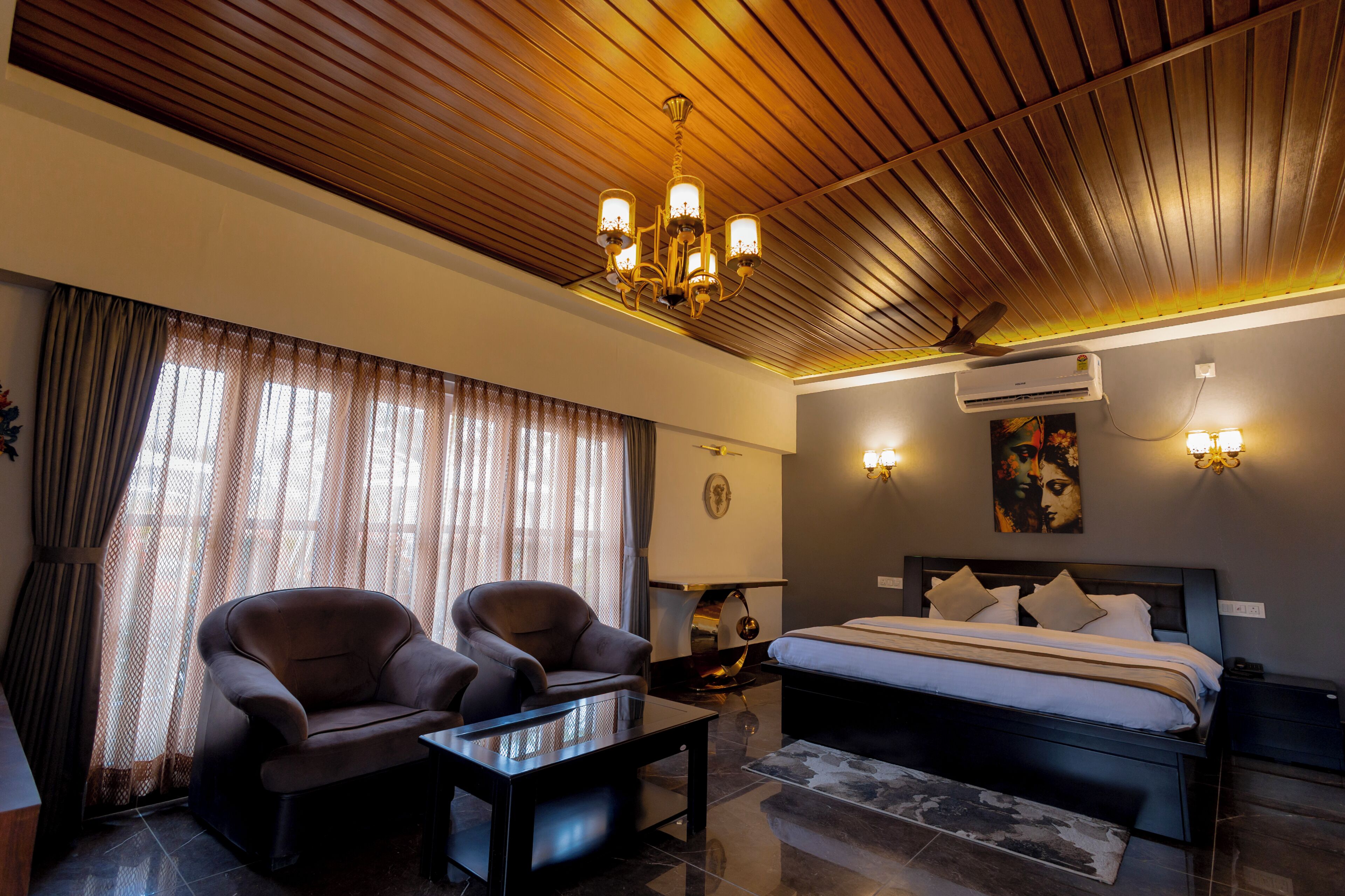 A hotel room with a bed, two armchairs, a coffee table, a ceiling fan, and wall-mounted lights.