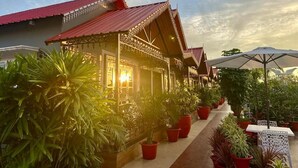 A traditional building with a red roof and ornate details, surrounded by potted plants and outdoor seating. - YKC FARMS AND VILLA (Siliguri)